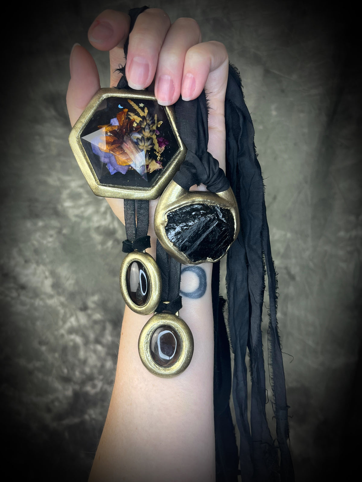 A hand holding various protection crystal necklaces hung from leather and silk. Fall wardrobe jewelry staples for the gemstone boho crowd. Handmade in Baltimore MD by Become Spellbound.