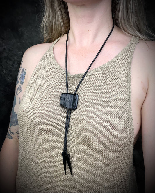 Black tourmaline crystal bolo tie with black spike tips on black leather, gothic statement jewelry for protection and grounding, handmade in Baltimore Maryland. Modeled here to show size.