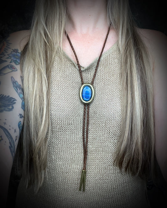 Blue flash labradorite bolo tie with brown leather cord, gold finish, and decorative sunburst bolo tips. Handmade by Become Spellbound.