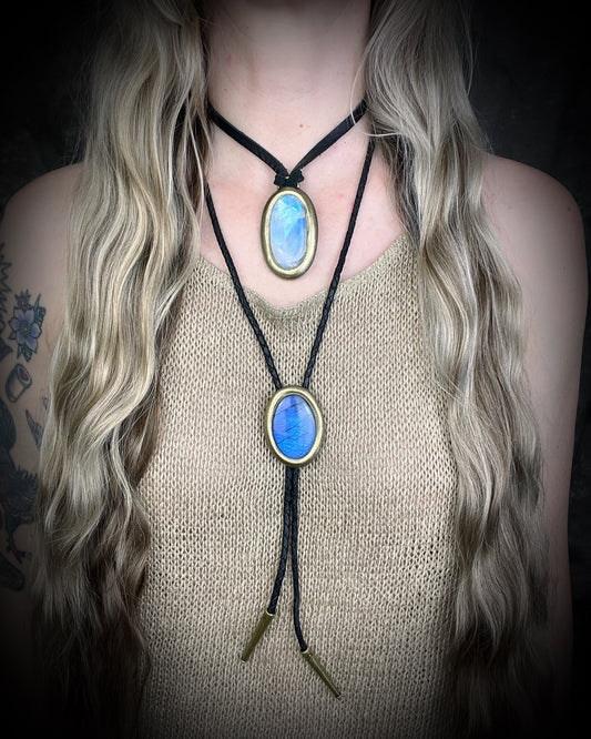 Person wearing a bolo tie with blue labradorite stone pendant layered with a rainbow moonstone necklace on a dark background