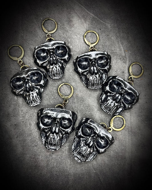 Flat lay of black skull earrings with brass hooks — handmade gothic earrings with sculptural detail.