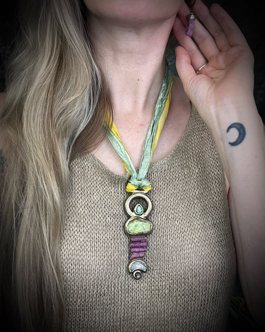 Fully hand sculpted Libyan Desert Glass talisman pendant with raw ruby crystals, prasiolite moon, lepidolite, green tourmaline, and luminous shifting color on recycled silk. Museum grade art jewelry by Become Spellbound.