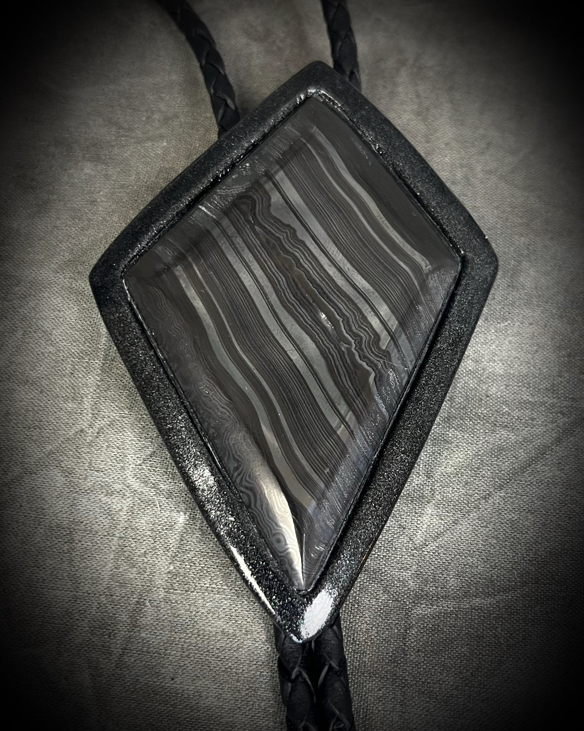 Genuine asymmetrical kite-shaped psilomelane bolo tie with black finish, black leather cord, and black spike bolo tips. Handmade by Become Spellbound.