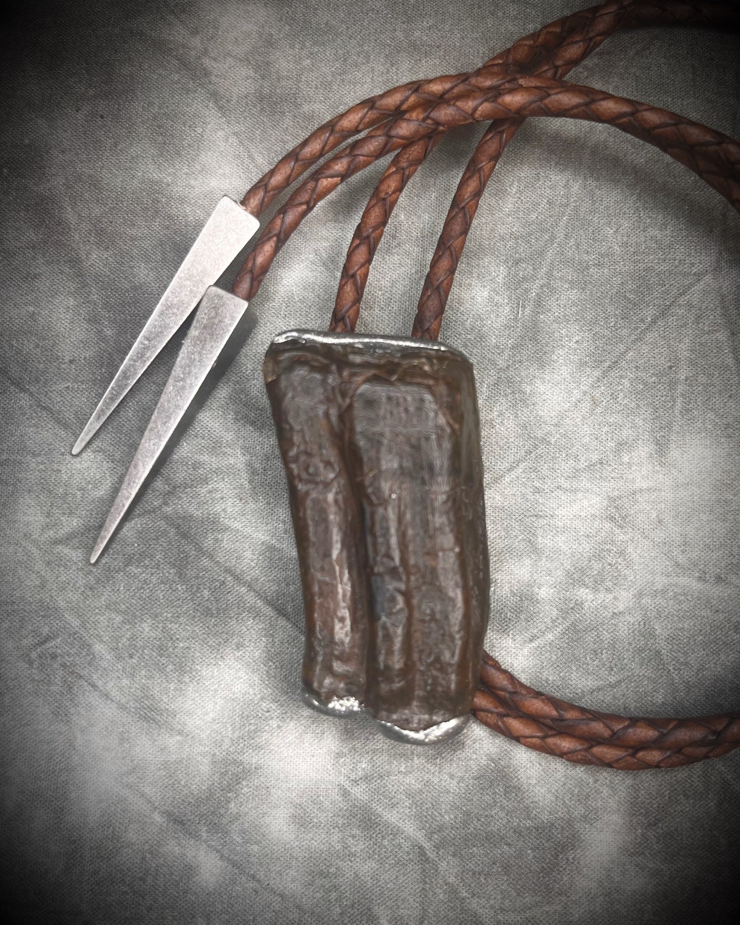 Handmade Equus bolo tie featuring horse tooth fossil centerpiece with gunmetal silver sculptural detailing, brass findings, spike tip ends, and leather cord bolo necklace. Natural history talisman for him, handmade in Baltimore Maryland.