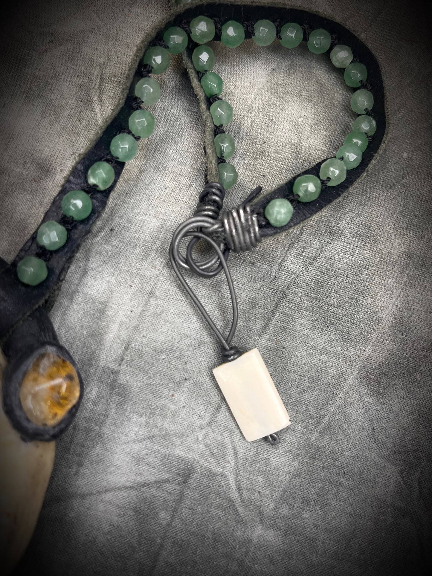 Handmade leather talisman with quartz, bloodstone, citrine, green aventurine, animal teeth, studded leather, and handmade wire clasp by Anothai Hansen.