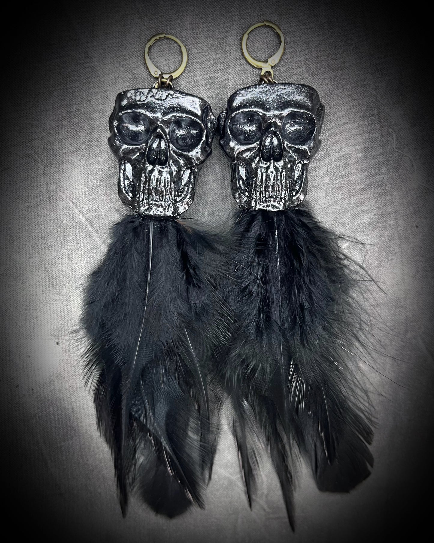 Handmade black skull and black feather earrings in a vintage inspired brass or sterling silver huggy earring style. Witchy and boho style meets gothic elegance.