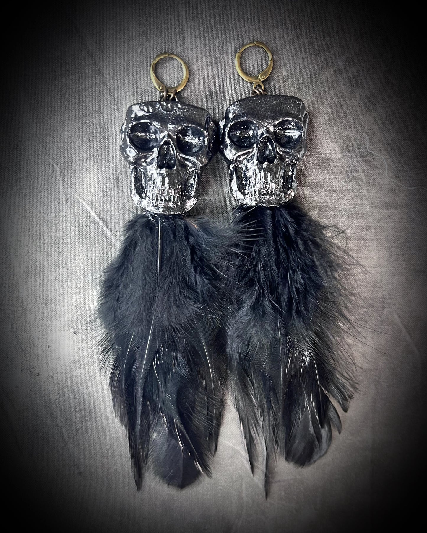 Handmade black skull and black feather earrings in a vintage inspired brass or sterling silver huggy earring style. Witchy and boho style meets gothic elegance.