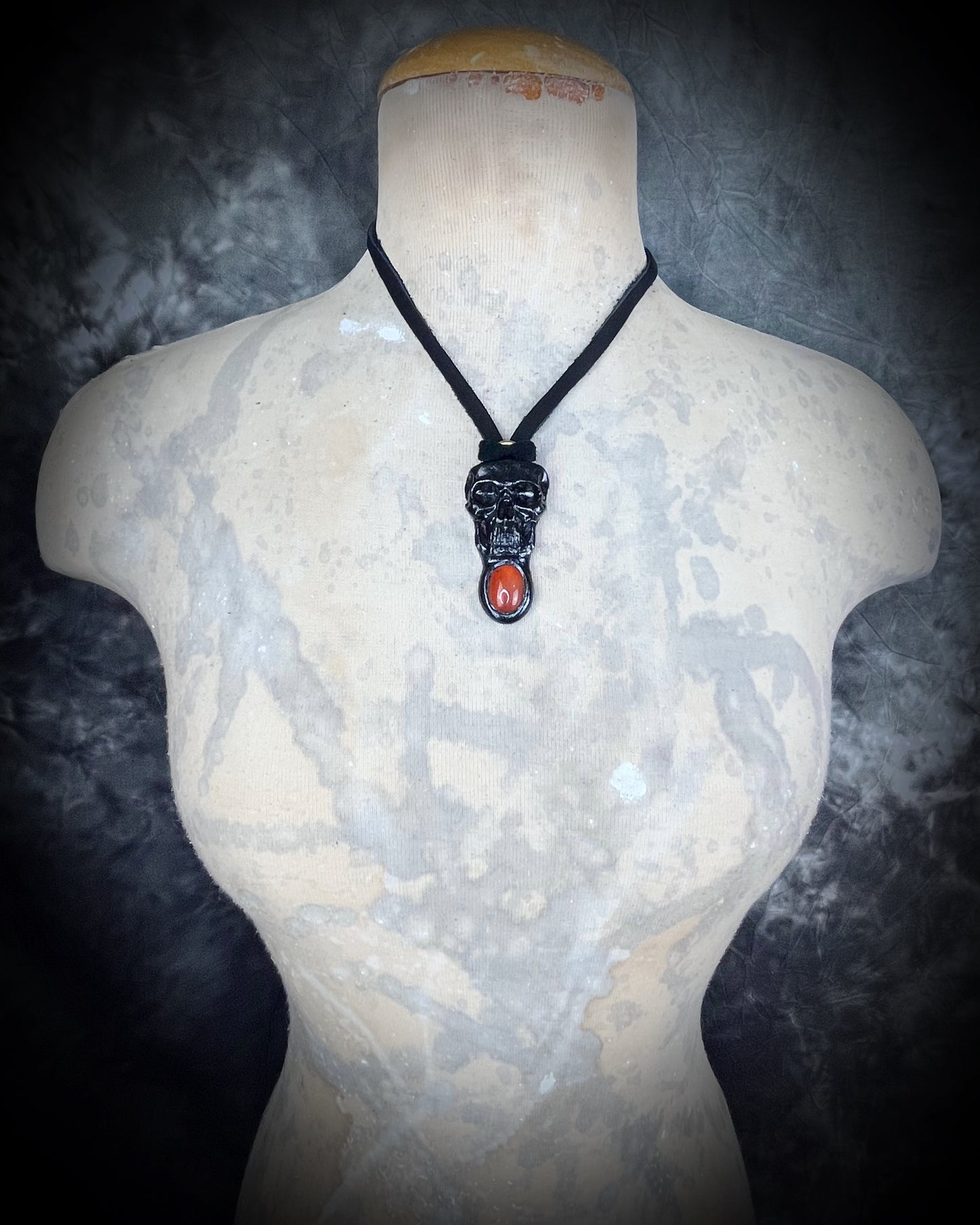Mannequin wearing black skull and orange carnelian crystal talisman on black leather cord, gothic and mystical jewelry for fall, cosplay, renaissance festival, handcrafted statement necklace.