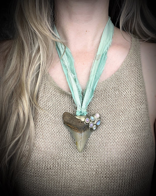 Megalodon fossil shark tooth talisman necklace with rainbow moonstone, lavender spinel, and pink tourmaline gemstones on sea green recycled silk, handmade statement fossil jewelry with oceanic boho elegance from Baltimore Maryland.