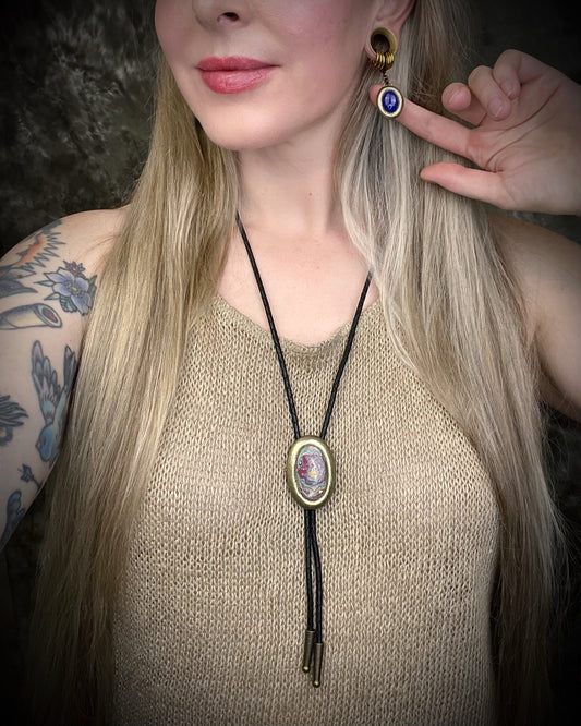 Model wearing Cadillac Ranch Fordite manmade colorful swirling gemstone Bolo tie set in a gold finish and mounted on soft black bolo leather. A talisman for the modern man, crystal jewelry for him. Western 2026 jewelry trend bolo.