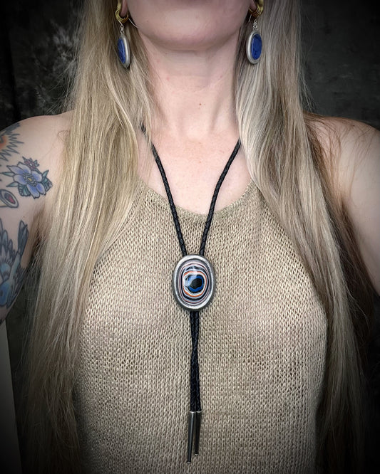 Model wearing Fordite manmade colorful swirling gemstone Bolo tie set in a gunmetal silver finish and mounted on soft black bolo leather. A talisman for the modern man, crystal jewelry for him. Western 2026 jewelry trend bolo.