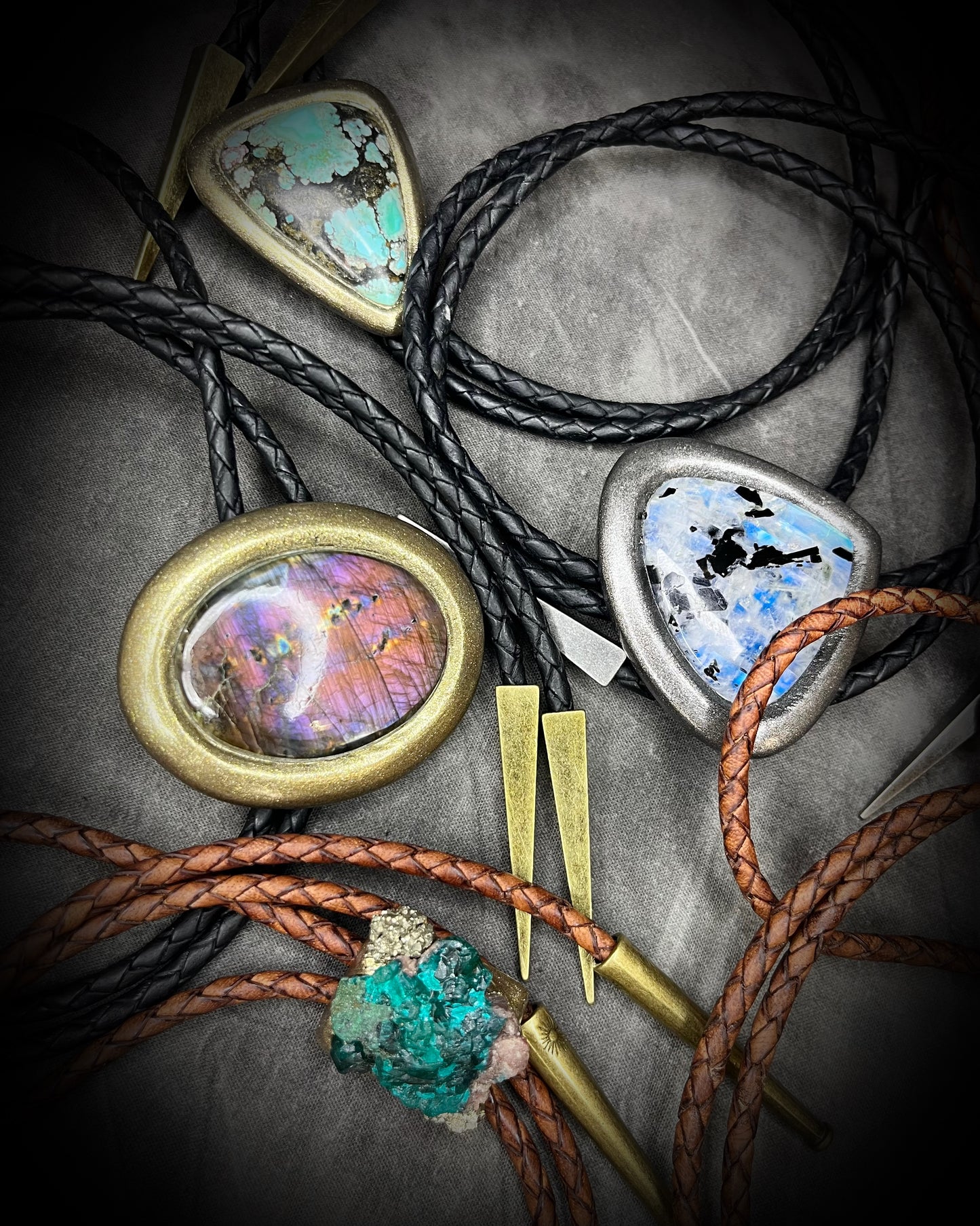 Mystical crystal bolo ties with gold and silver finishes and black and brown leather on a textured background. Handmade western gift for him.