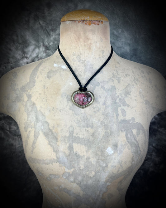 Rhodonite crystal necklace with a heart-shaped pink and black gemstone pendant on a mannequin bust against a dark background