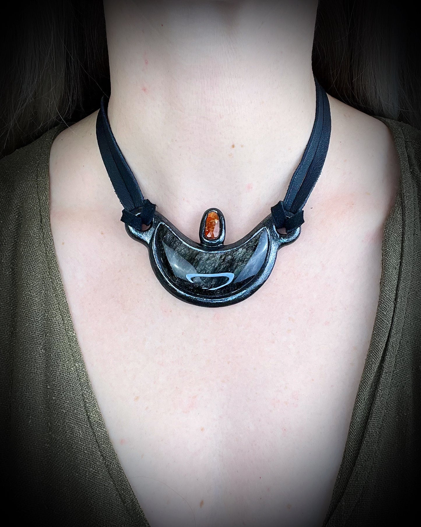 Silver Sheen obsidian crescent moon necklace with orange kyanite crystal. Dark luxury vibe gemstone necklace hung from black leather for a unisex goth look.