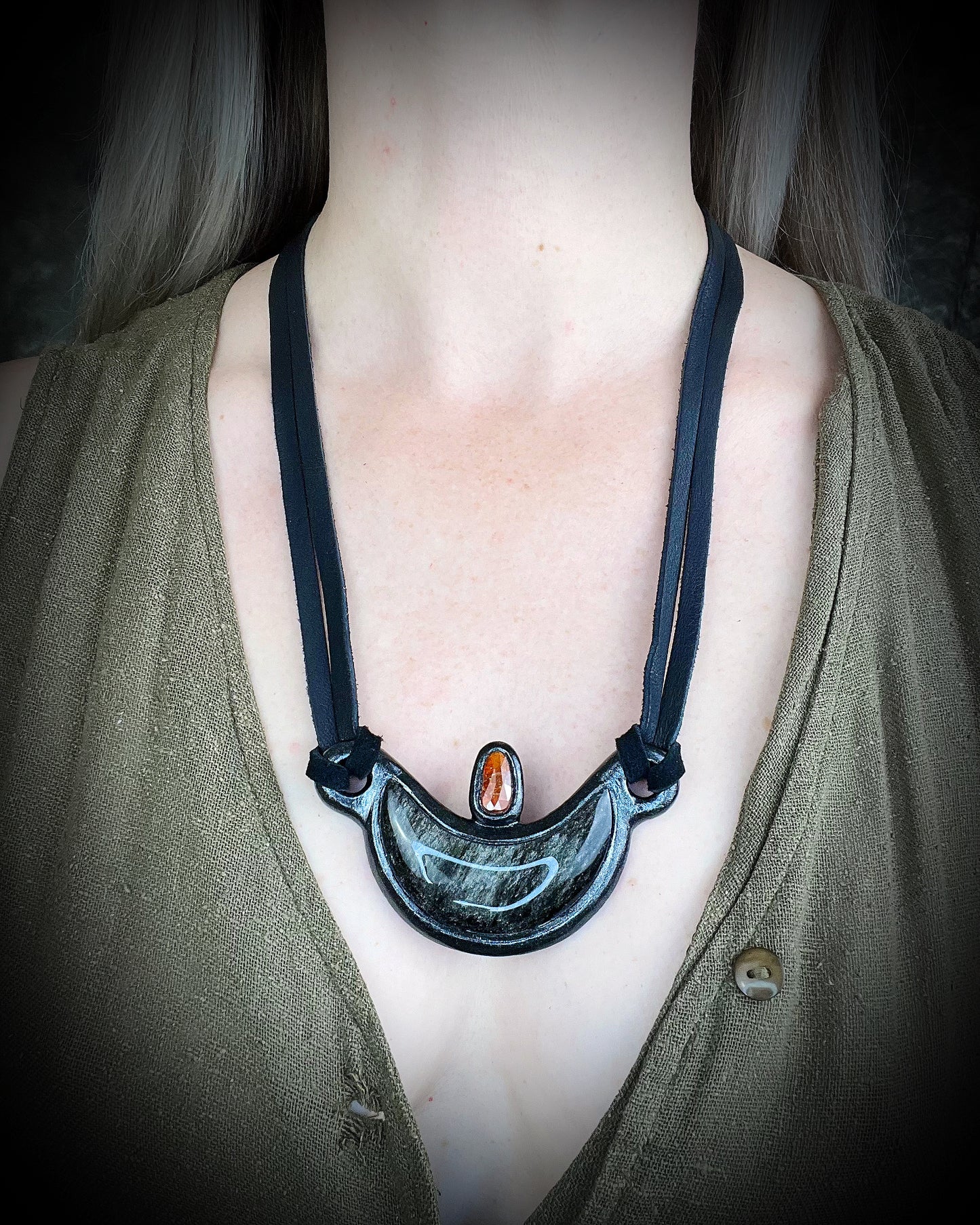 Silver Sheen obsidian crescent moon necklace with orange kyanite crystal. Dark luxury vibe gemstone necklace hung from black leather for a unisex goth look.
