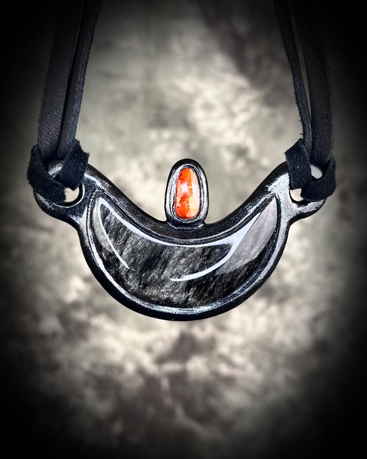 Silver Sheen obsidian crescent moon necklace with orange kyanite crystal. Dark luxury vibe gemstone necklace hung from black leather for a unisex goth look.