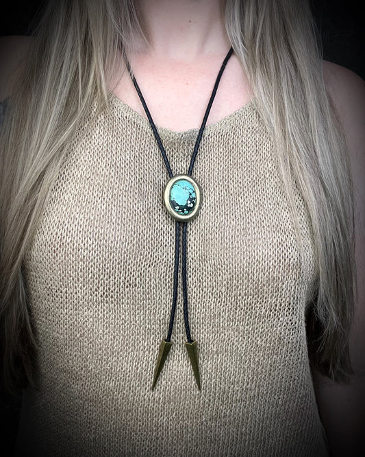 Turquoise bolo tie necklace in gold finish on black leather with spike tips, artisan Western statement jewelry with crystal focal stone, handmade in Baltimore Maryland. Shown here on a model