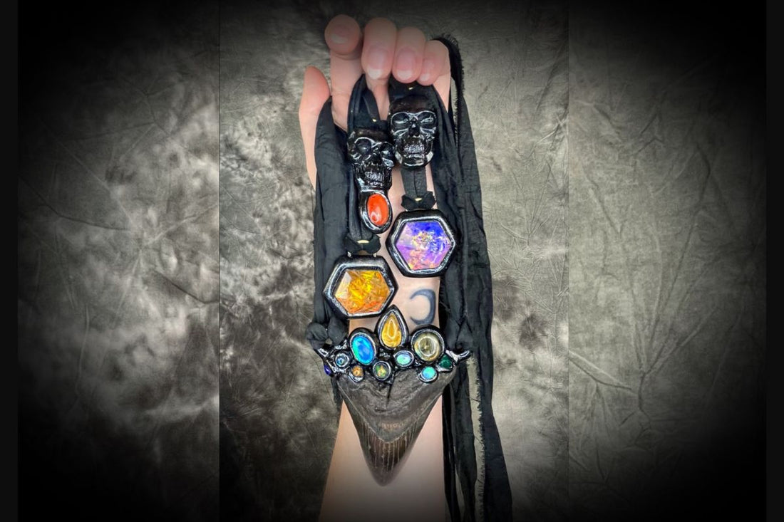 A hand holding several gothic gemstone necklaces hung from black leather or recycled silk. skull necklaces and glowing crystal pendants.