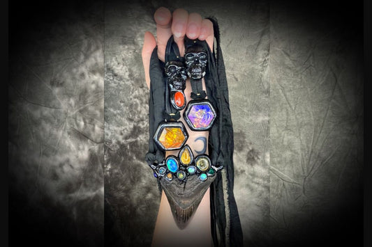 A hand holding several gothic gemstone necklaces hung from black leather or recycled silk. skull necklaces and glowing crystal pendants.