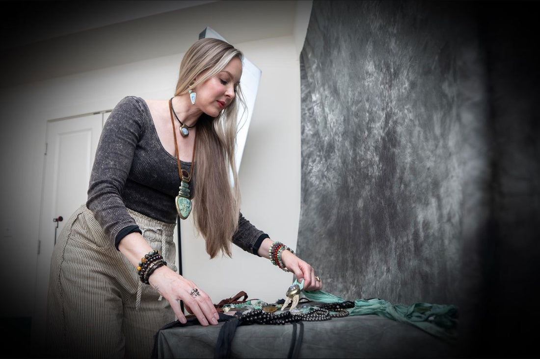 Baltimore Based Jewelry Designer Kari Dern is arranging a flat lay of her crystal jewelry on a table with a photo backdrop under and behind it, selecting the top crystal trends she is noticing in 2026. 