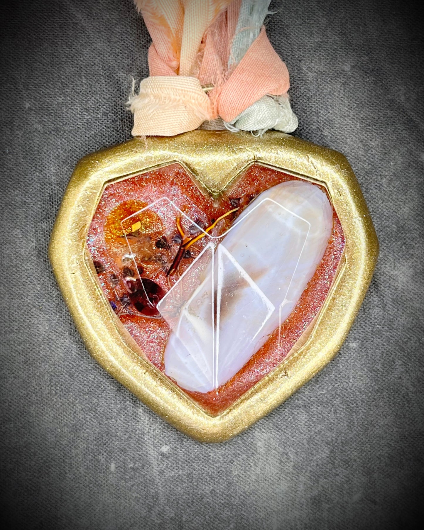 Heart-shaped pendant with gold frame and embedded stone on a textured gray background