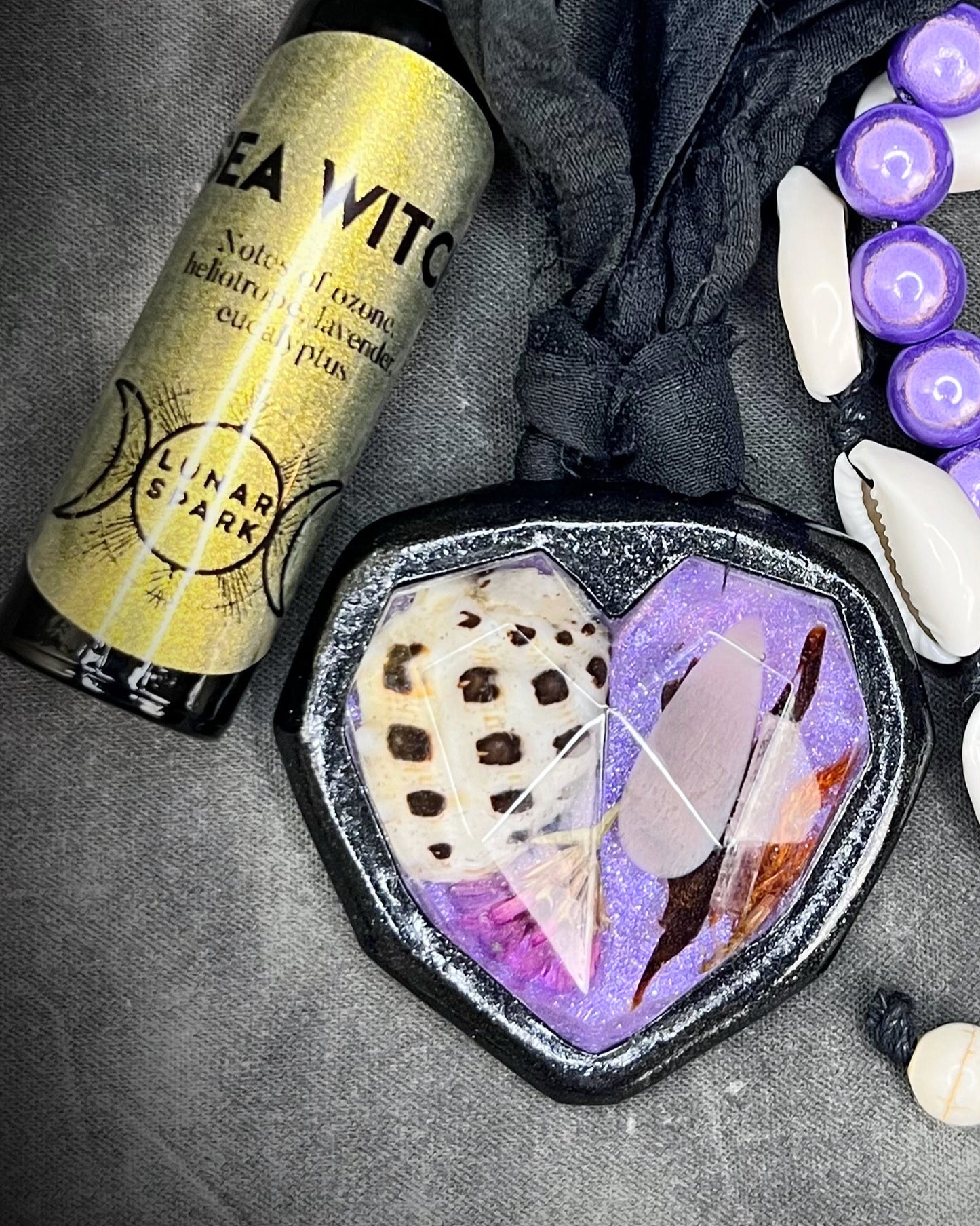 Perfume bottle labeled 'Sea Witch', and decorative shell necklace on a dark surface.