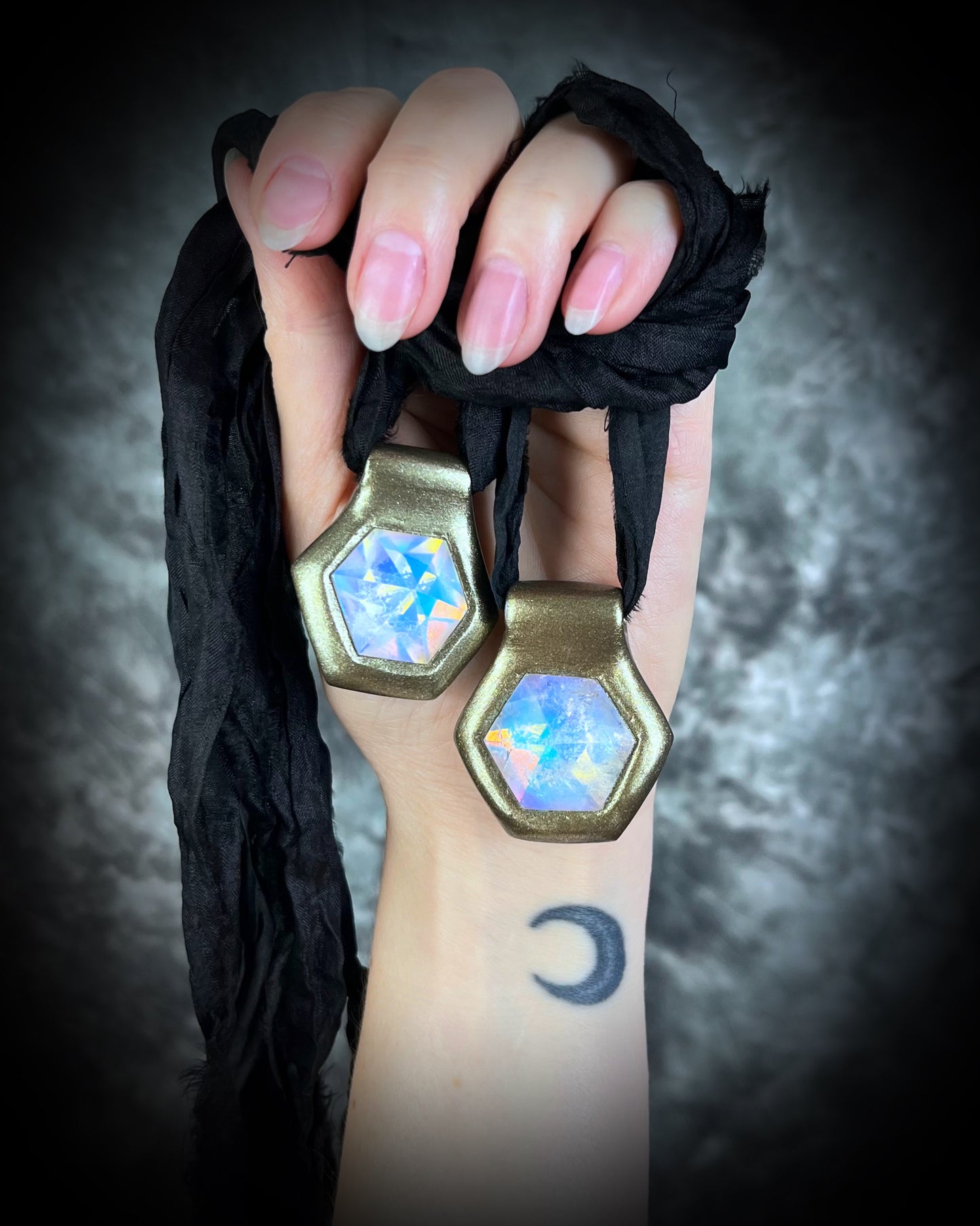 Shown here held in a hand with natural nails, Handmade designer clear opalescent quartz gemstone pendants in a gold finish.  These crystal healing pyramid hexagon necklaces are strung from black recycled silk for the sustainable and eco-friendly jewelry lover, boho babe or modern mystic. 