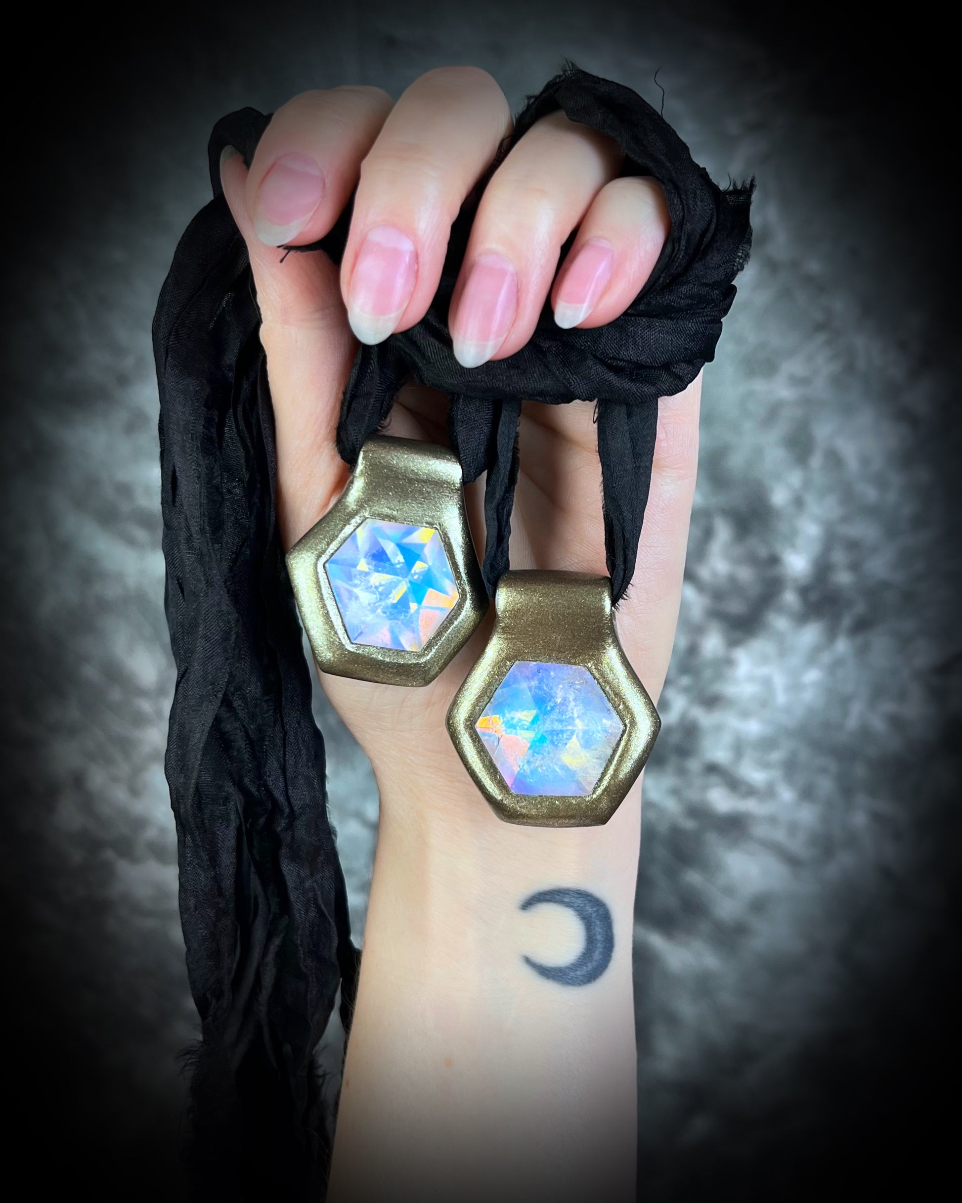 Shown here held in a hand with natural nails, Handmade designer clear opalescent quartz gemstone pendants in a gold finish.  These crystal healing pyramid hexagon necklaces are strung from black recycled silk for the sustainable and eco-friendly jewelry lover, boho babe or modern mystic. 