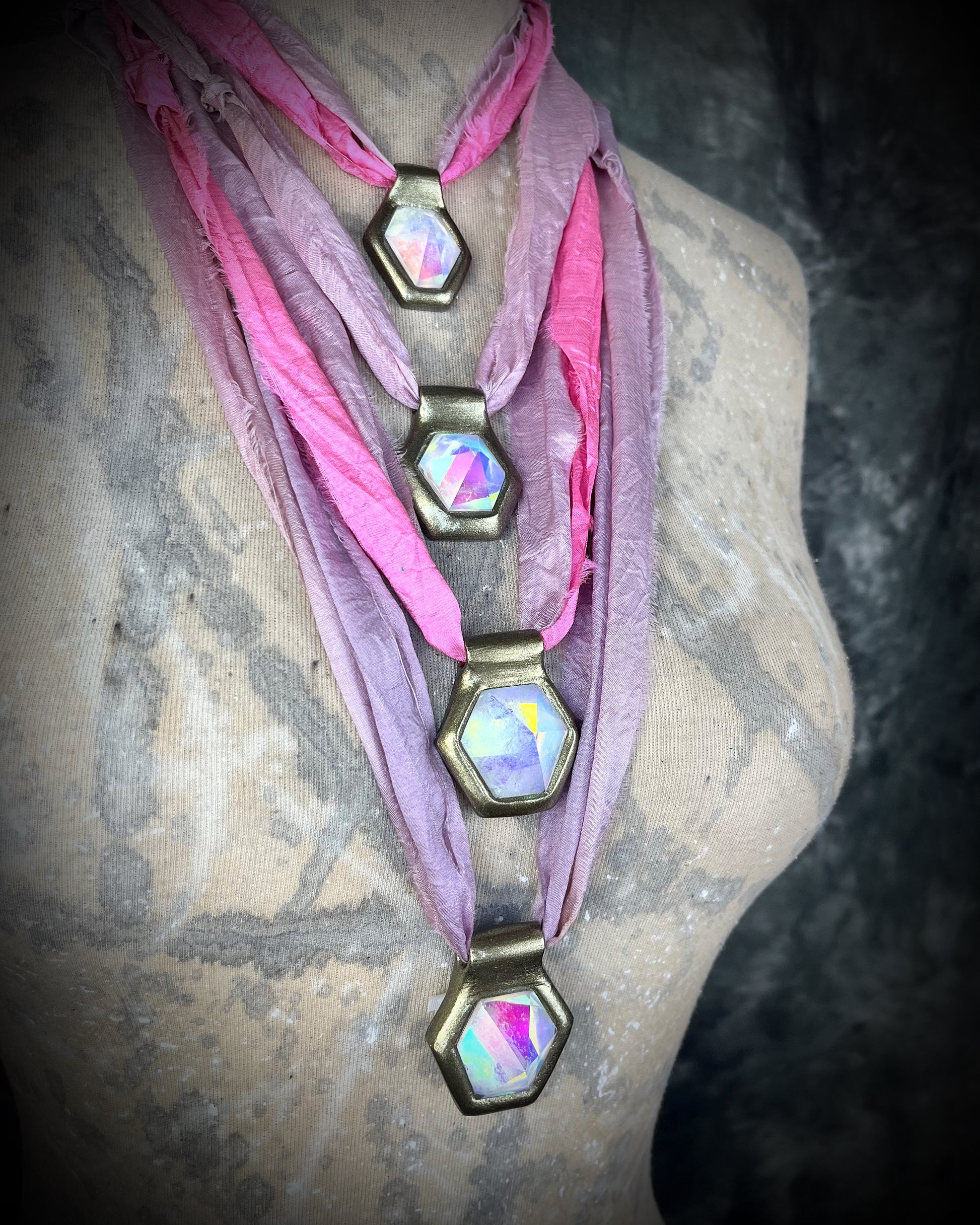 Handmade designer clear opalescent quartz gemstone pendants in a gold finish.  These crystal healing pyramid hexagon necklaces are strung from lilac and pink recycled silk for the sustainable and eco-friendly jewelry collector. 