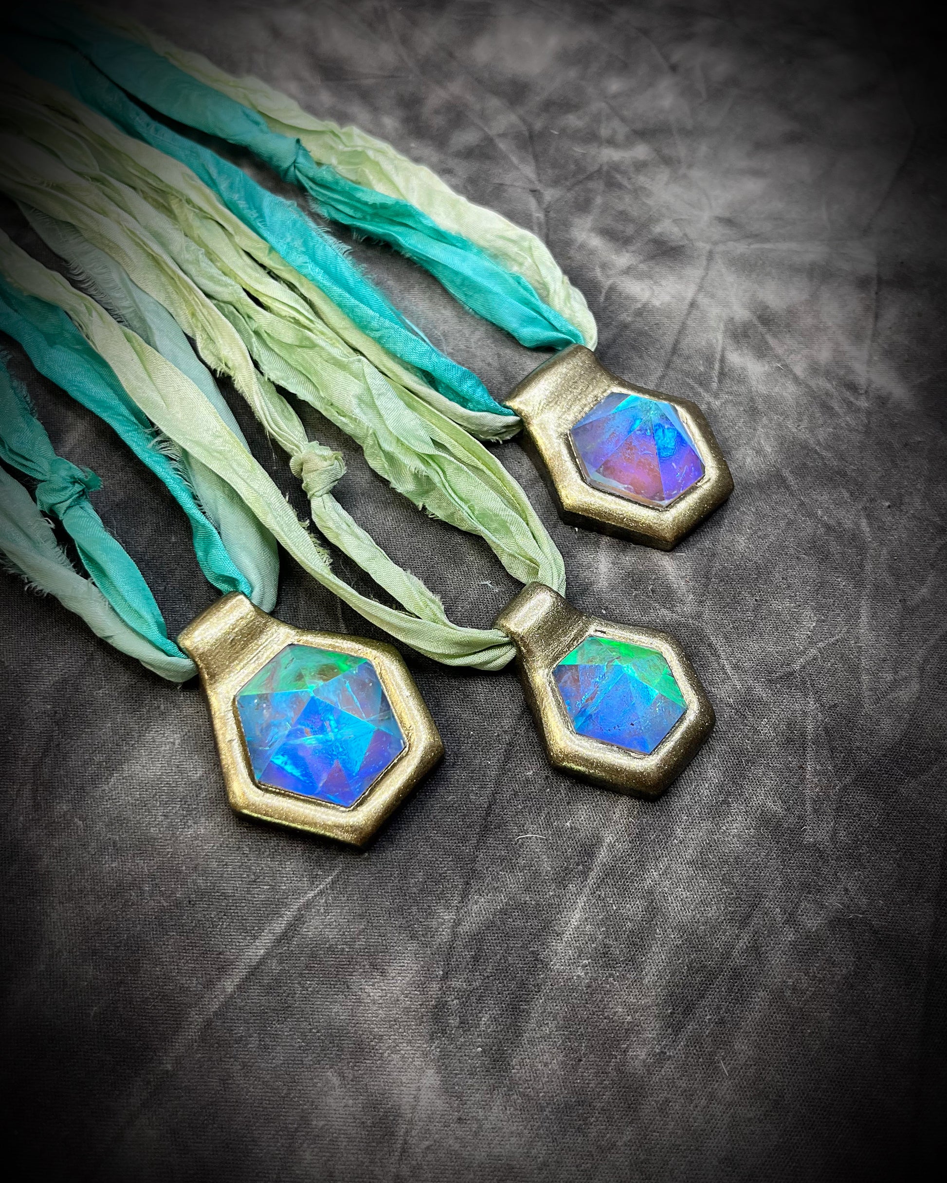 Side view of purple handmade designer aqua turquoise opalescent quartz gemstone pendants in a gold finish.  These crystal healing necklaces are customizable and can be strung from leather or sea green recycled silk for the sustainable and eco-friendly jewelry lover or mermaid.