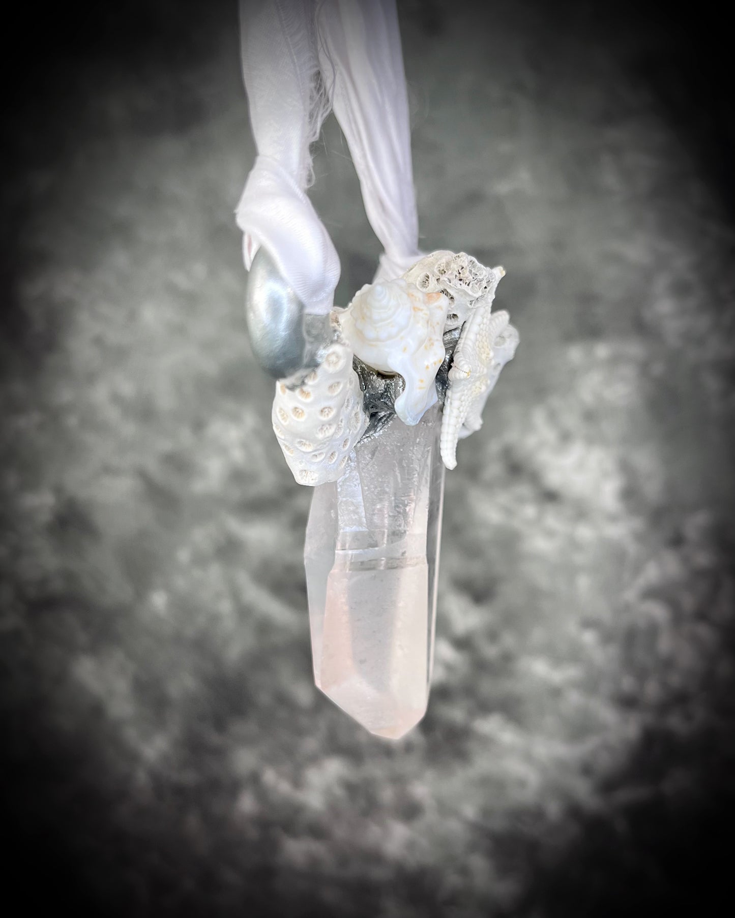 Angle view of silver handmade designer bridal or beach bride necklace featuring quartz crystal, white fossilized coral, starfish, seashell and is strung from recycled white silk for an eco-friendly summer beach wedding elegance.  