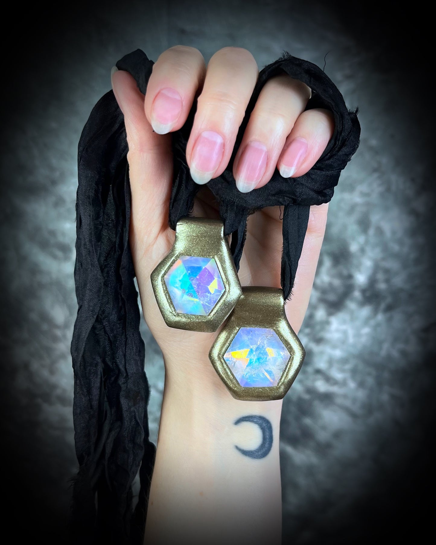 Shown here held in a hand with natural nails, Handmade designer clear opalescent quartz gemstone pendants in a gold finish.  These crystal healing pyramid hexagon necklaces are strung from black recycled silk for the sustainable and eco-friendly jewelry lover, boho babe or modern mystic. 