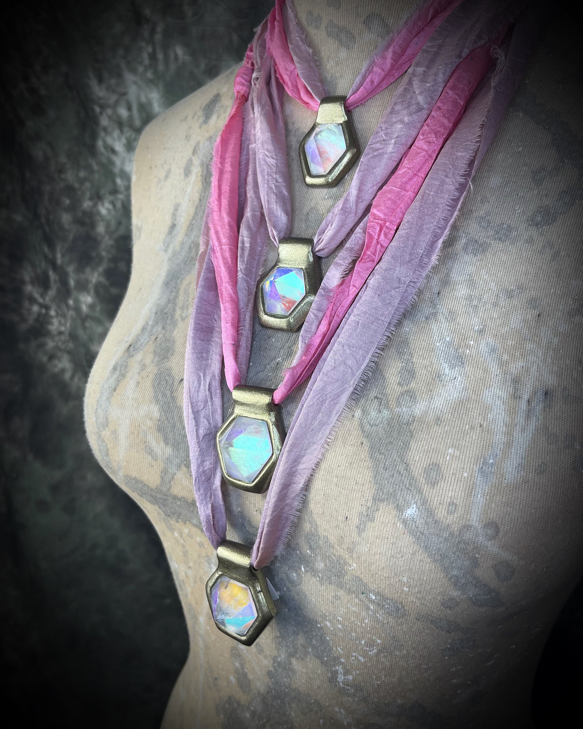 Closeup shot on mannequin of handmade designer clear opalescent quartz gemstone pendants in a gold finish.  These crystal healing pyramid hexagon necklaces are strung from lilac and pink recycled silk for the sustainable and eco-friendly jewelry collector. 
