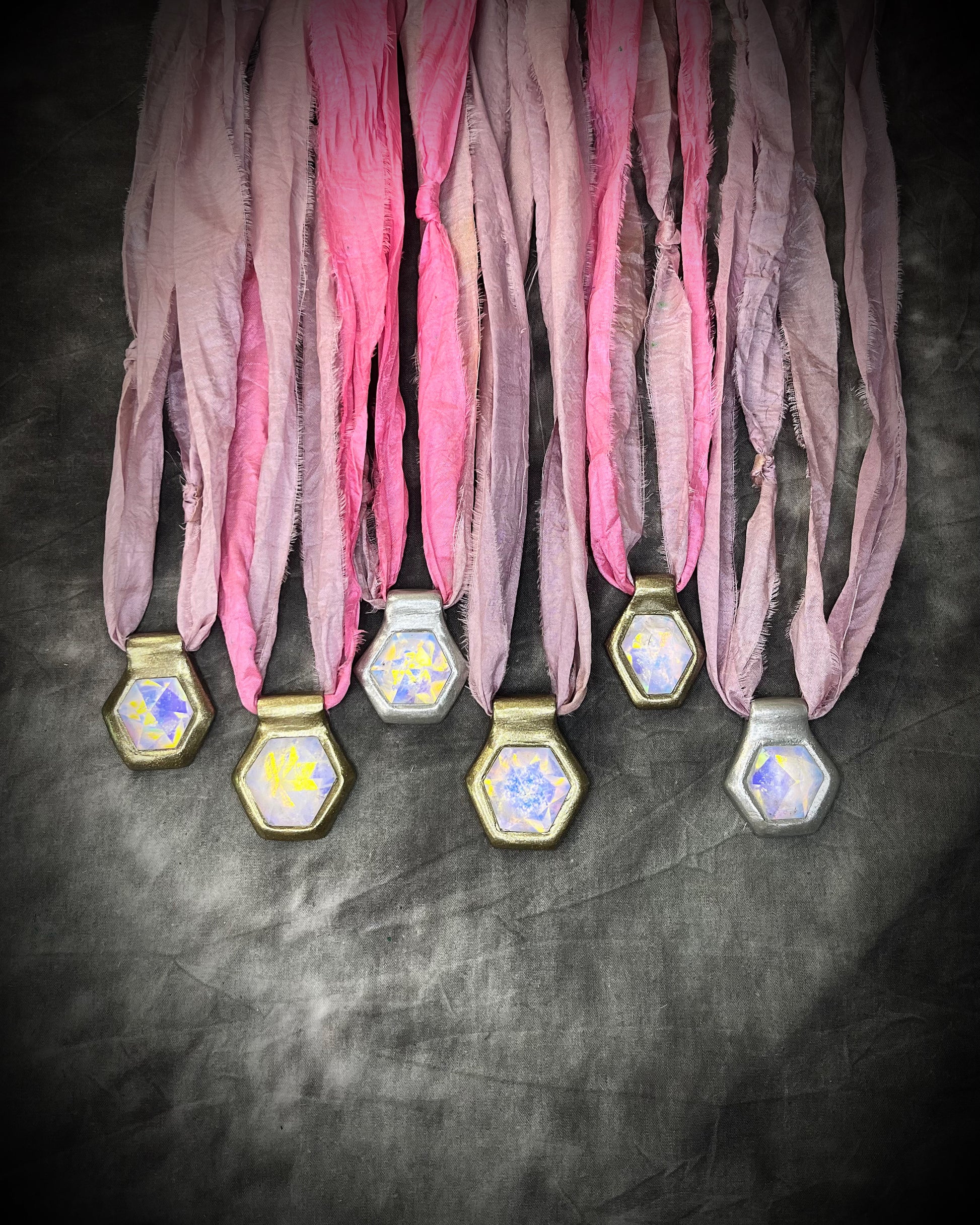 Many handmade designer clear opalescent quartz gemstone pendants in a gold and silver finish.  These crystal healing pyramid hexagon necklaces are strung from lilac and pink recycled silk for the sustainable and eco-friendly jewelry collector. 