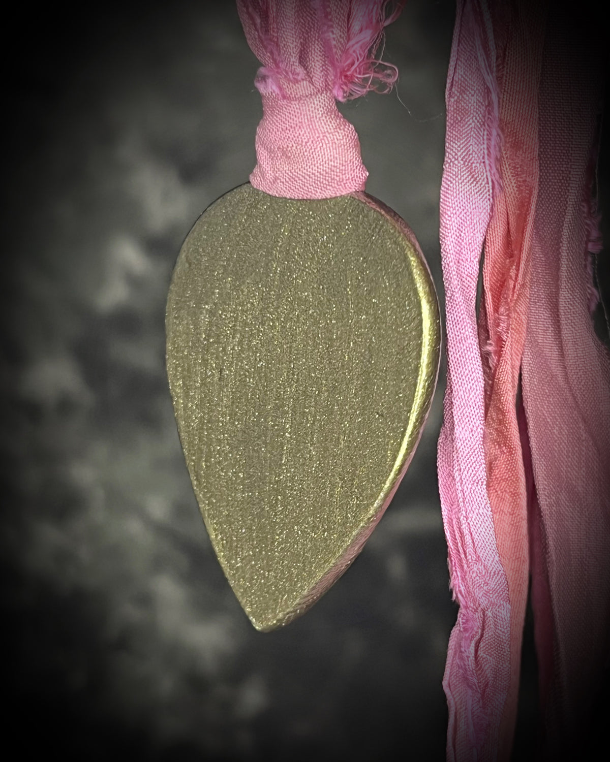 A teardrop-shaped pendant with a gold  border and a pink and white marbled pink calcite stone inside, hanging from a pink recycled silk ribbon. Heart chakra crystals for love and healing. 