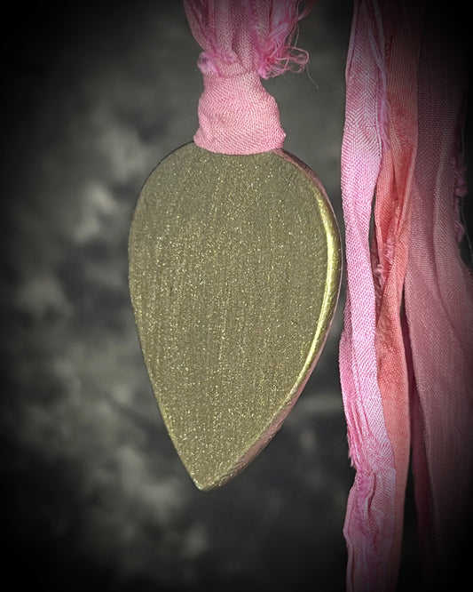 A teardrop-shaped pendant with a gold  border and a pink and white marbled pink calcite stone inside, hanging from a pink recycled silk ribbon. Heart chakra crystals for love and healing. 