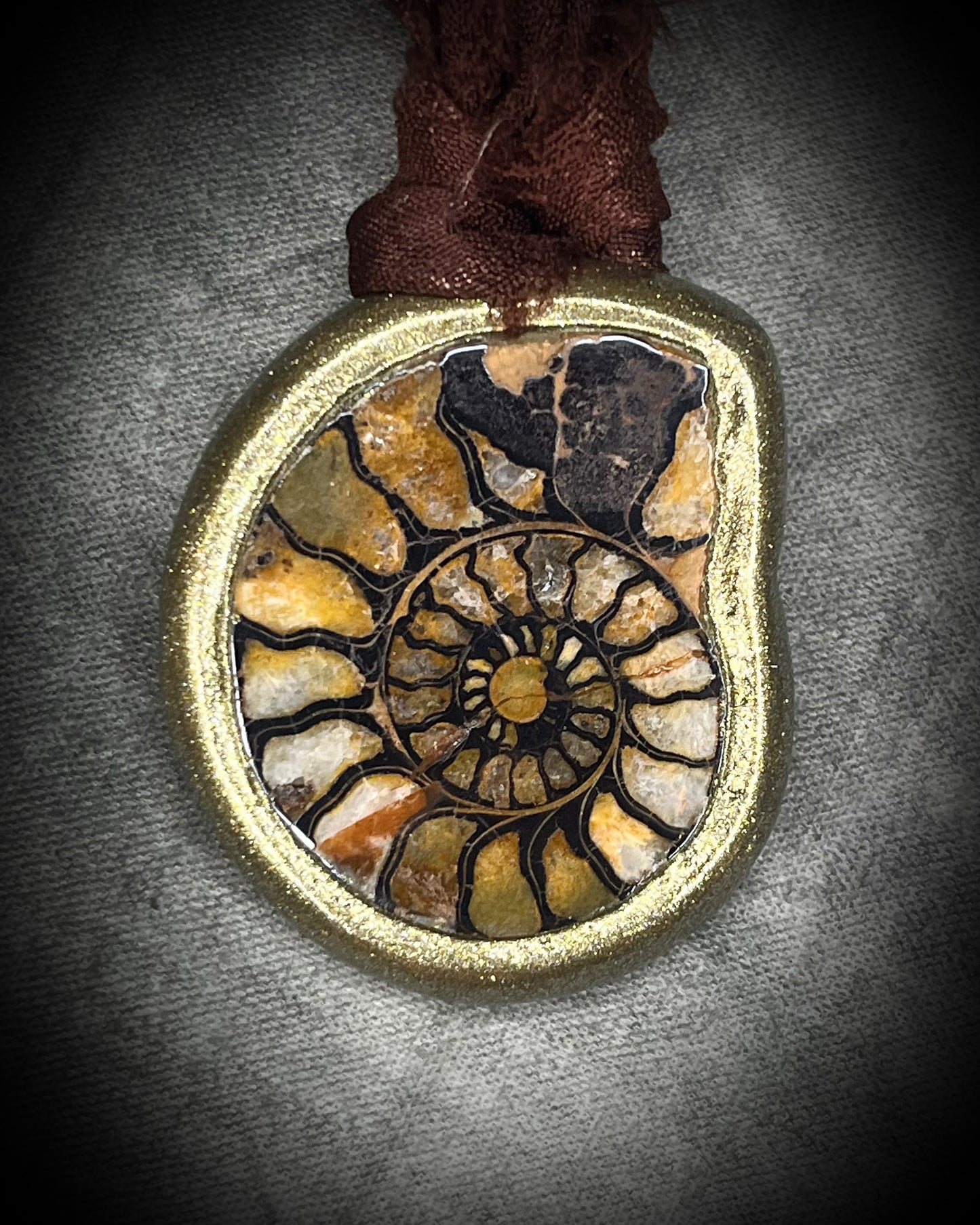 Ammonite fossil necklace featuring an ancient spiral fossil suspended from brown recycled silk, handmade by Become Spellbound in Baltimore, Maryland. 