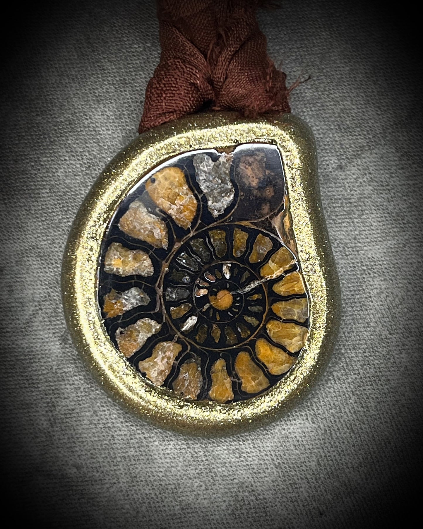 Ammonite fossil necklace featuring an ancient spiral fossil suspended from brown recycled silk, handmade by Become Spellbound in Baltimore, Maryland. 