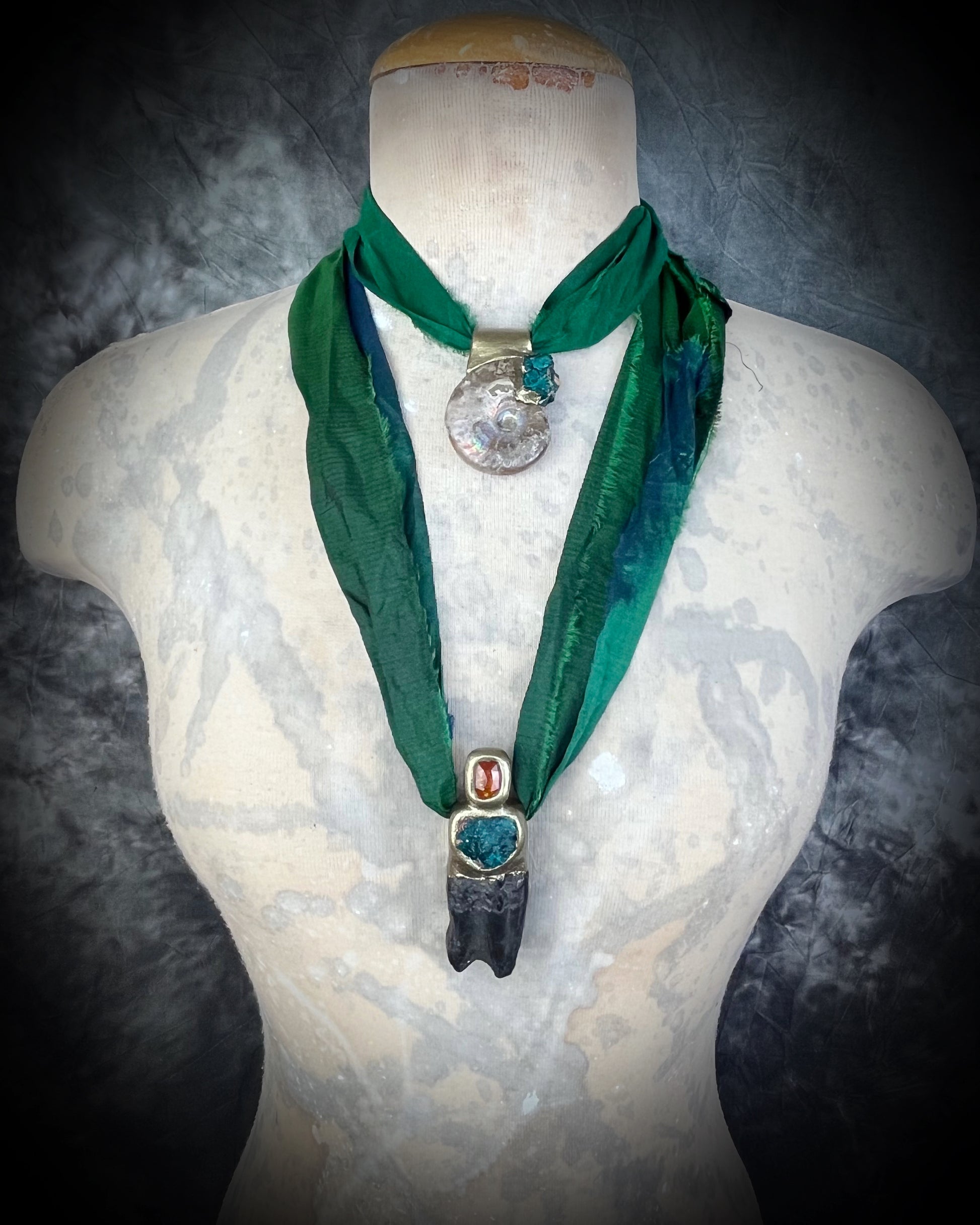 Ammonite fossil necklace with green dioptase crystals and Equus Horse tooth fossil necklace with orange kyanite gemstones. Both pendants are strung from eco-friendly green recycled silk and layered for 2025 fall maximalism and spiritual jewelry trends. 