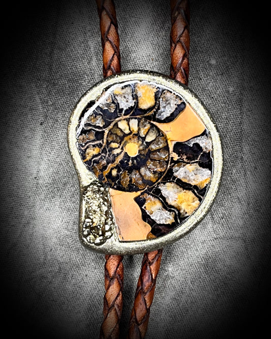 Closeup of Ammonite fossil with pyrite bolo tie on brown braided leather with brass tips — fantasy bohemian western jewelry.
