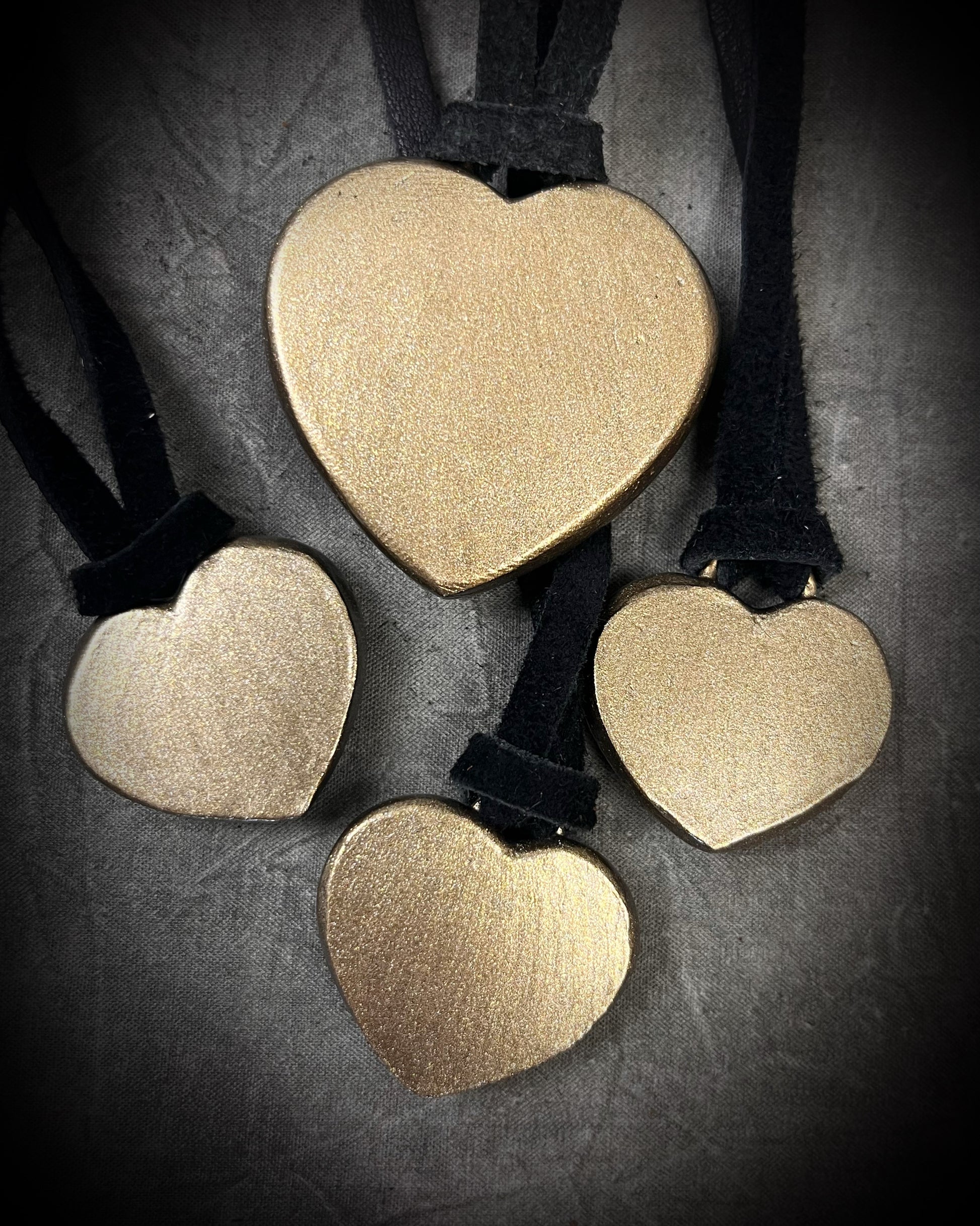 Back side of Several Mahogany obsidian heart pendant necklaces in gold finish on black leather in a flat lay arrangement of 4. Grounding protection crystal jewelry symbolizing strength and resilience. Gift for her.