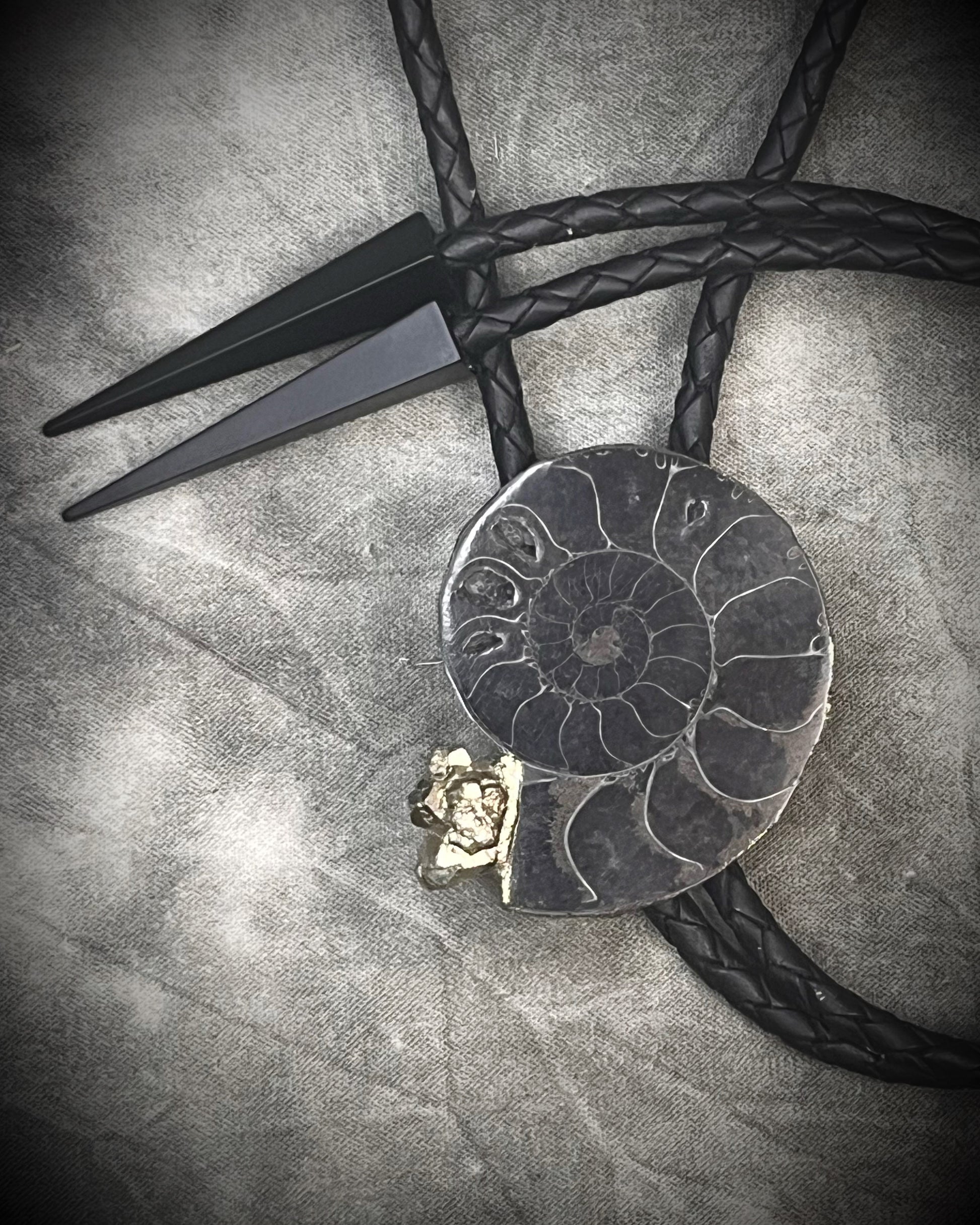 Black ammonite fossil and pyrite bolo tie for men on black leather with black spike tips, Western gothic statement jewelry with fossil and crystal detail, handmade in Baltimore Maryland.