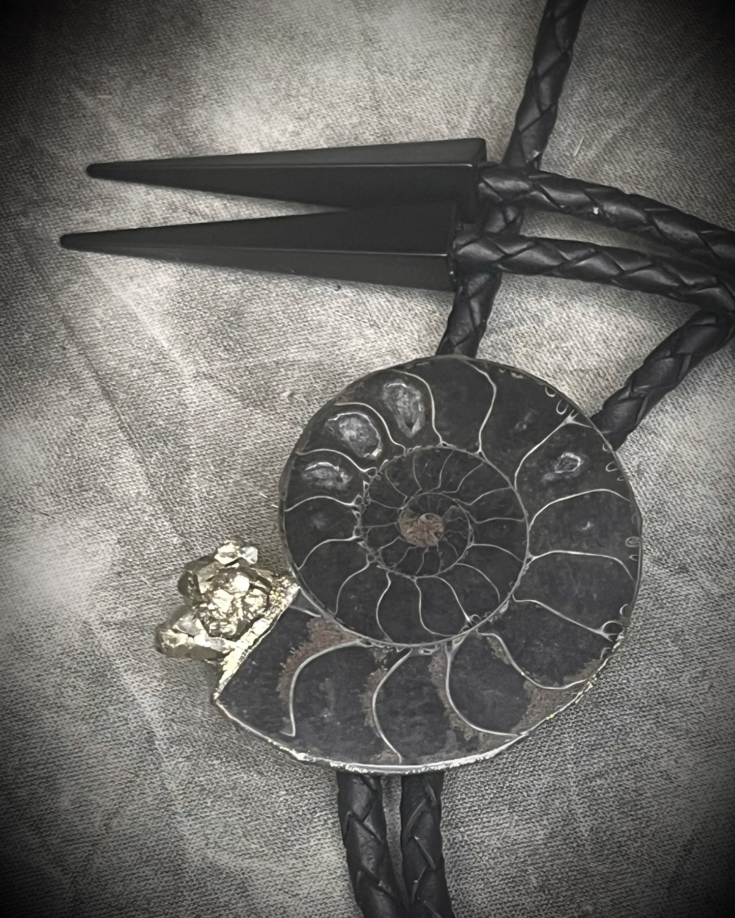 Black ammonite fossil and pyrite bolo tie for men on black leather with black spike tips, Western gothic statement jewelry with fossil and crystal detail, handmade in Baltimore Maryland.