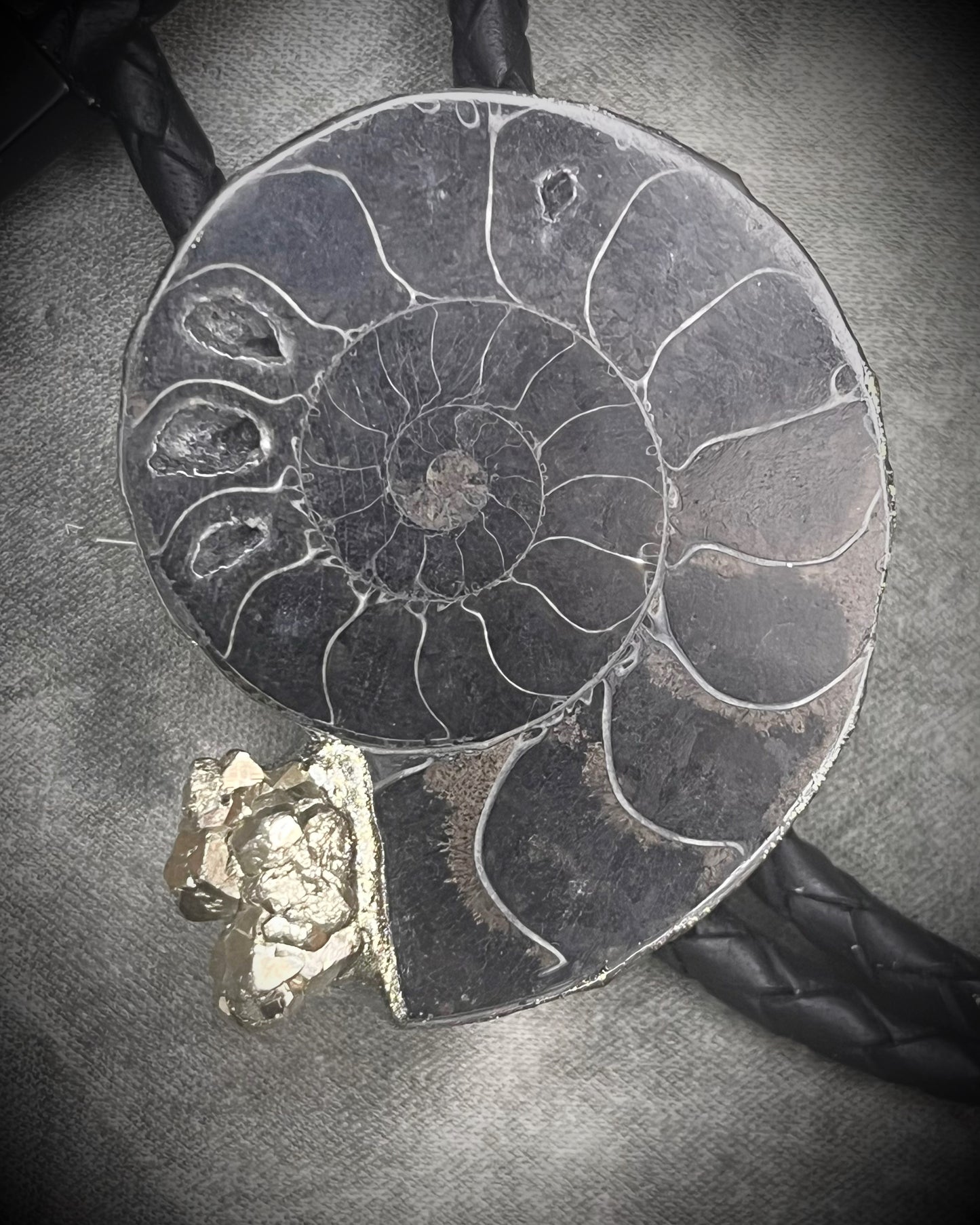 Black ammonite fossil and pyrite bolo tie for men on black leather with black spike tips, Western gothic statement jewelry with fossil and crystal detail, handmade in Baltimore Maryland. Closeup.