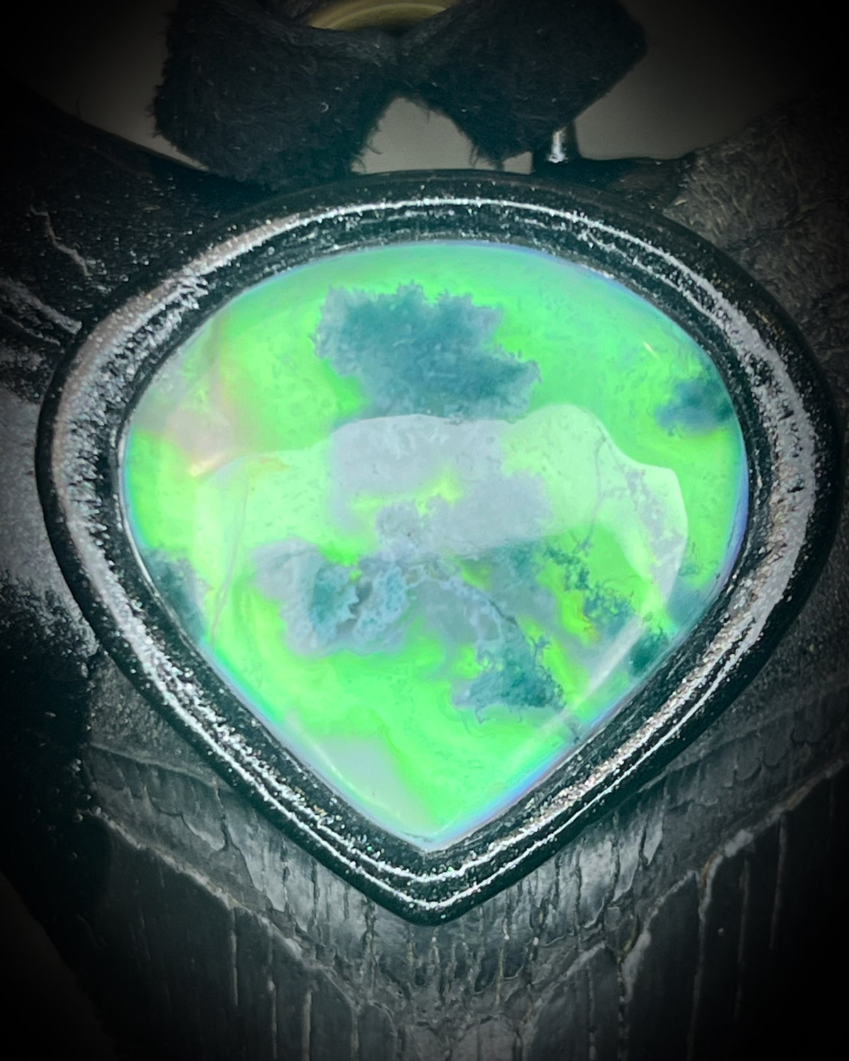 Black megalodon tooth talisman with a glowing green moss agate teardrop focal stone in a sculptural black-finish setting on black leather, handmade by Become Spellbound in Baltimore, Maryland.