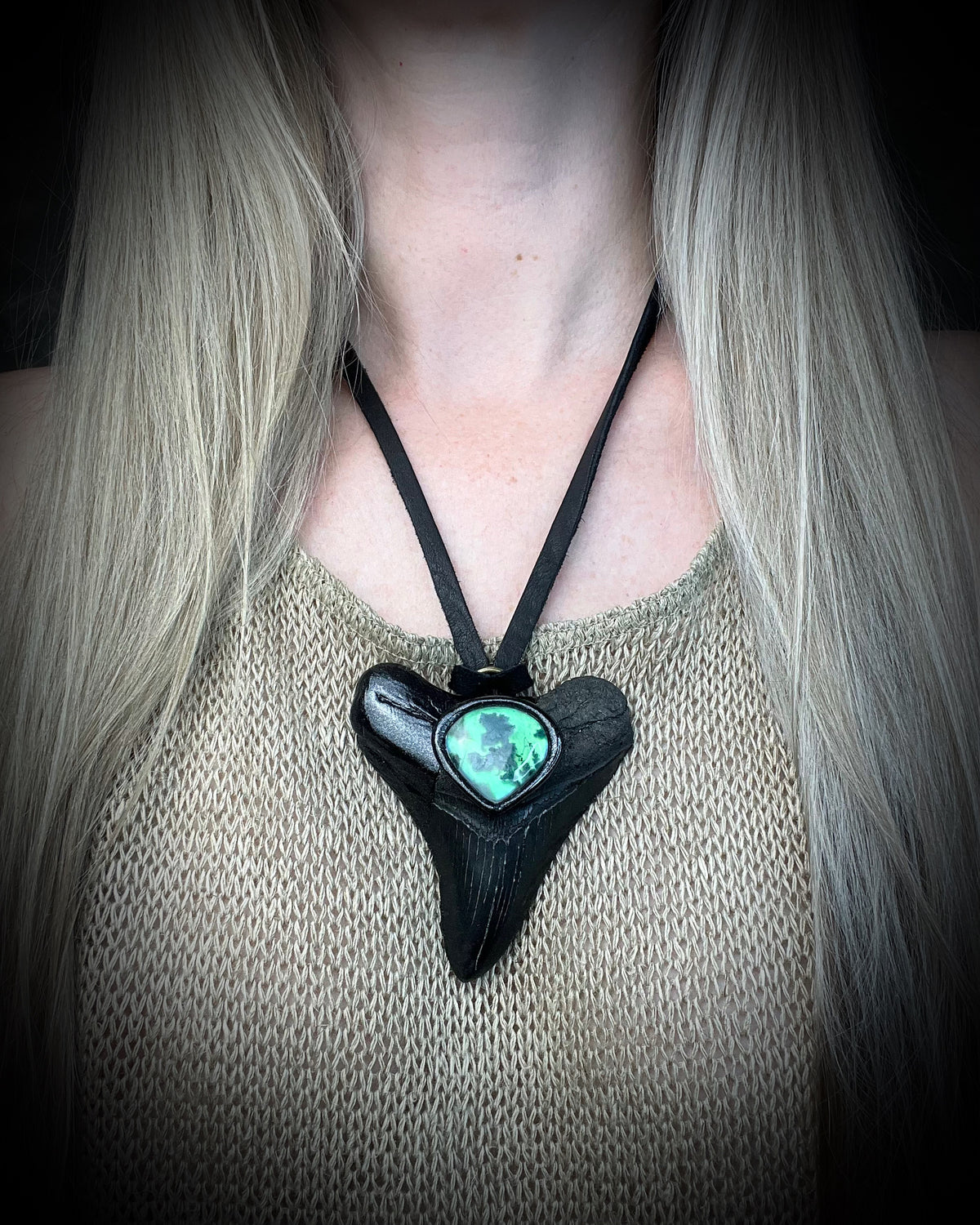 Black megalodon tooth talisman with a glowing green moss agate teardrop focal stone in a sculptural black-finish setting on black leather, handmade by Become Spellbound in Baltimore, Maryland.