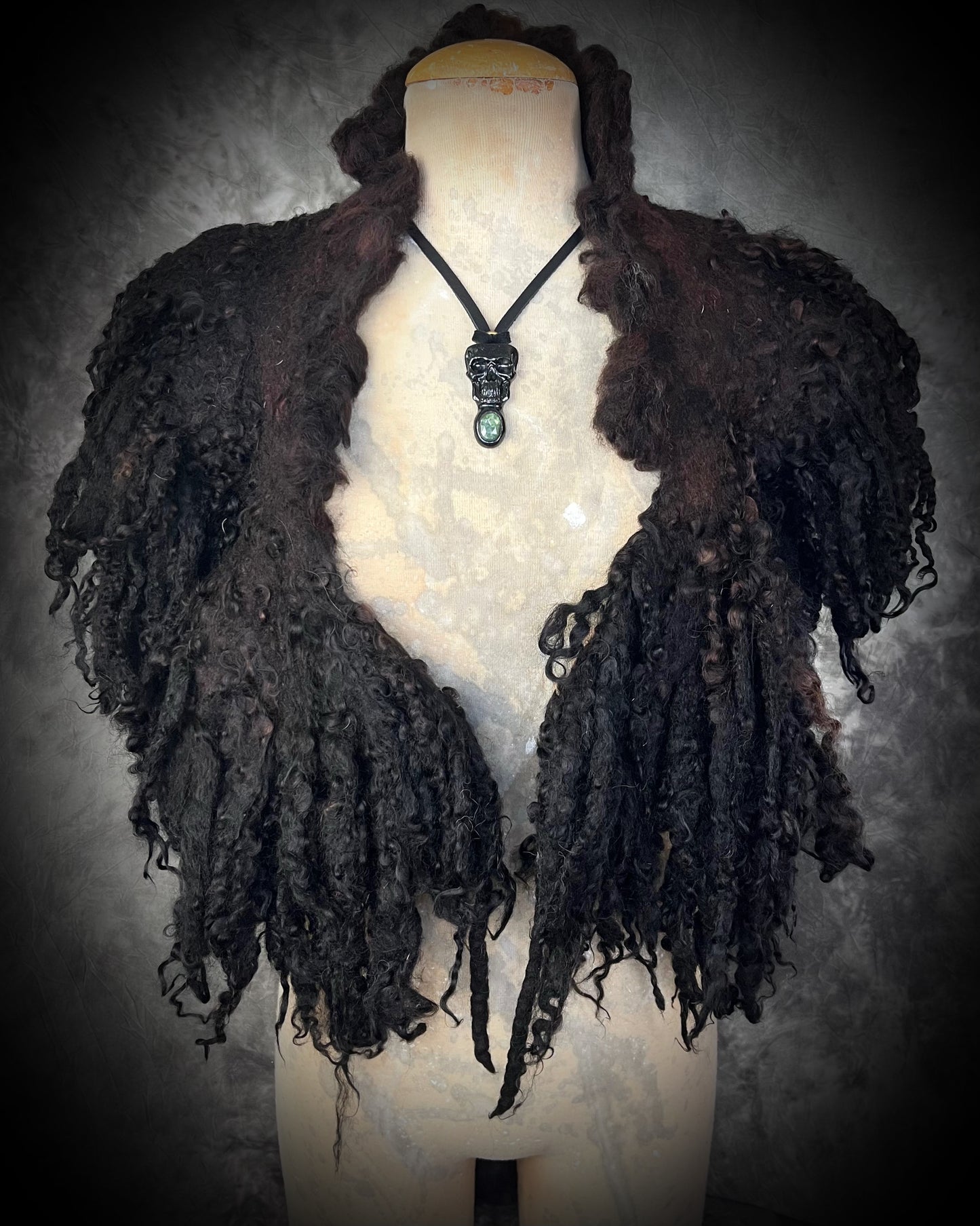 Black skull and green kyanite crystal necklace on black leather.  Worn on a bust with a black wooly handfelted curly cape. Macabre gothic jewelry for her, halloween gemstone jewelry for fall 2025 gift for him.