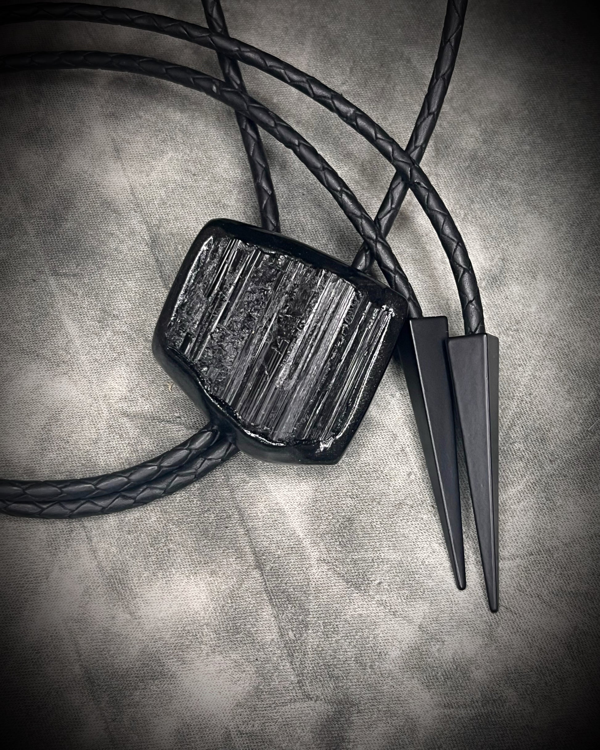 Black tourmaline crystal bolo tie with black spike tips on black leather, gothic statement jewelry for protection and grounding, handmade in Baltimore Maryland. 