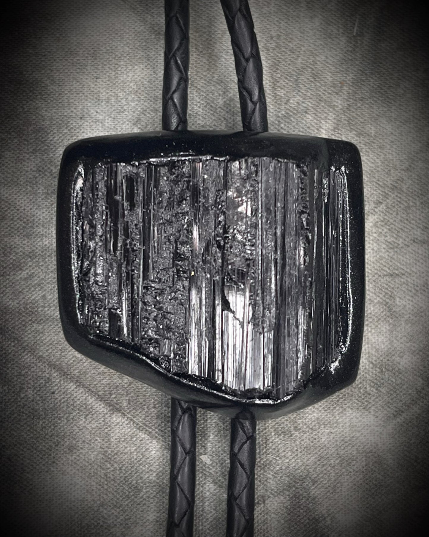 Black tourmaline crystal bolo tie with black spike tips on black leather, gothic statement jewelry for protection and grounding, handmade in Baltimore Maryland. Closeup.
