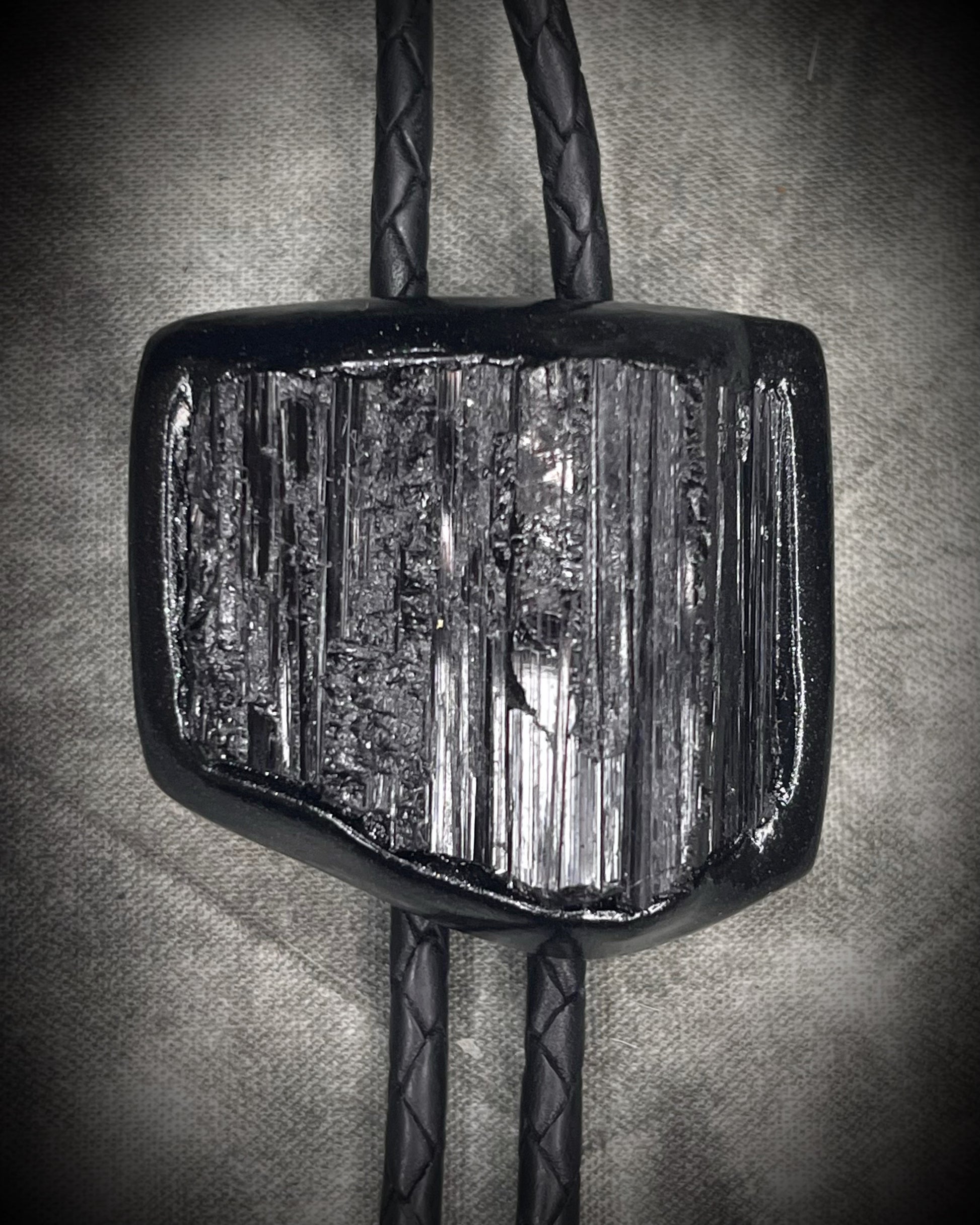 Black tourmaline crystal bolo tie with black spike tips on black leather, gothic statement jewelry for protection and grounding, handmade in Baltimore Maryland. Closeup.